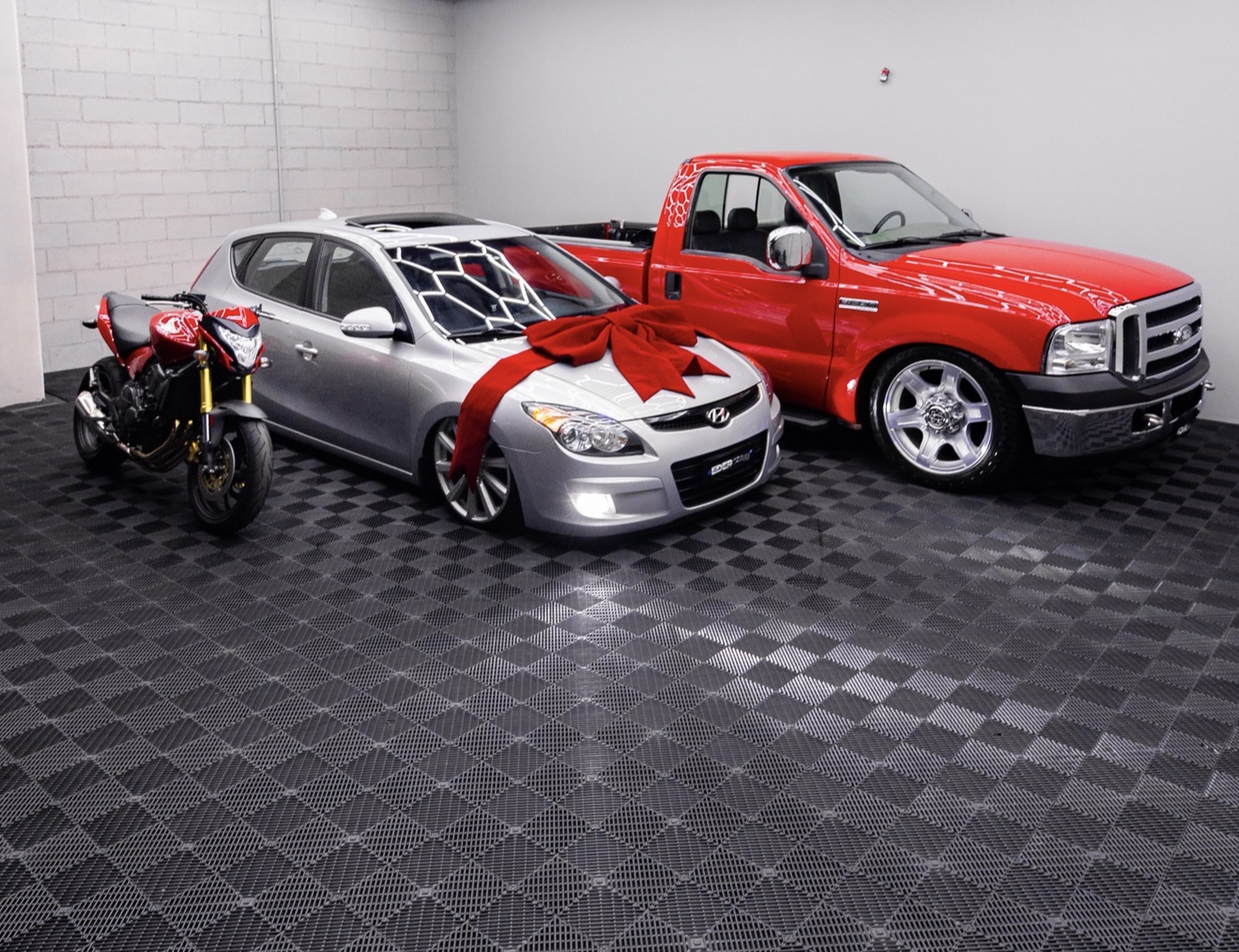 Picape vermelha, carro prata e motocicleta em showroom